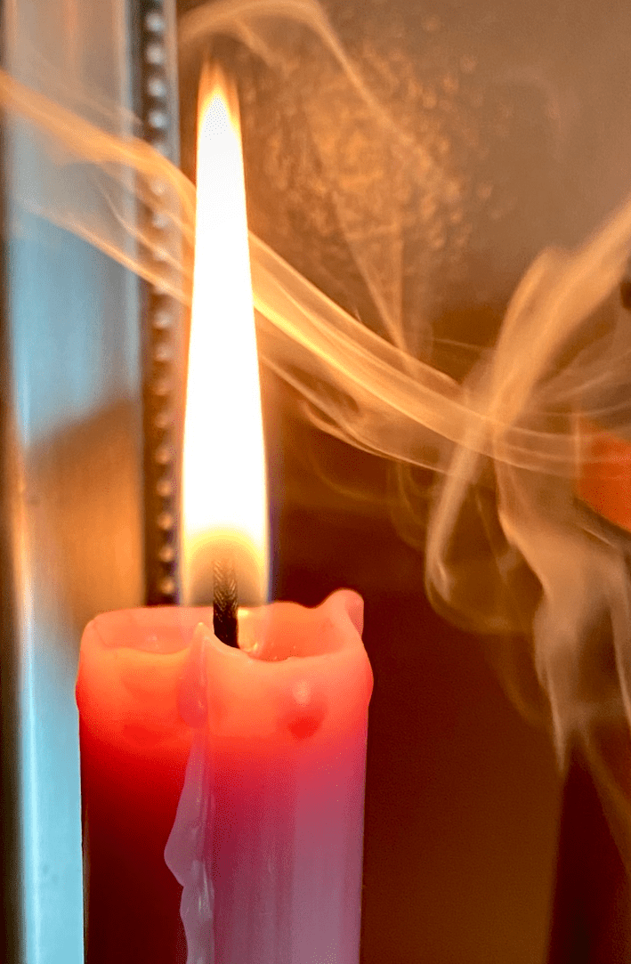 A mauve candle with a tall flame, surrounded by swirling smoke.